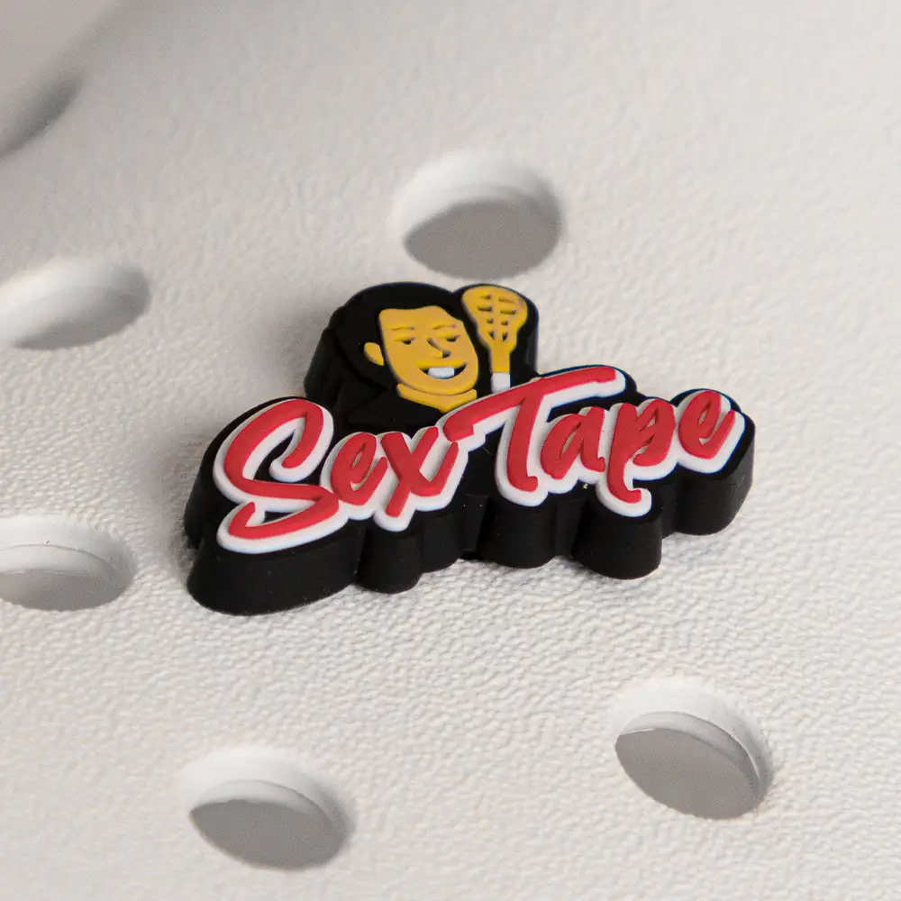 Close-up of Uncle Nicky’s Sex Tape lacrosse shoe charm attached to a white foam slide, featuring a 3D logo with mascot and red script lettering