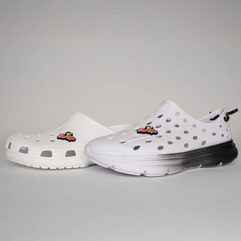 Two white foam slide-style shoes featuring Uncle Nicky’s Sex Tape 3D logo charms attached to the upper vents, styled on Croc and foam runner silhouettes